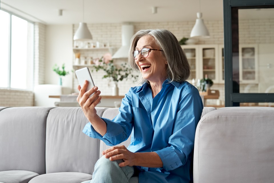 Ältere Dame mit einem Lächeln im Gesicht schaut auf ihr Smartphone